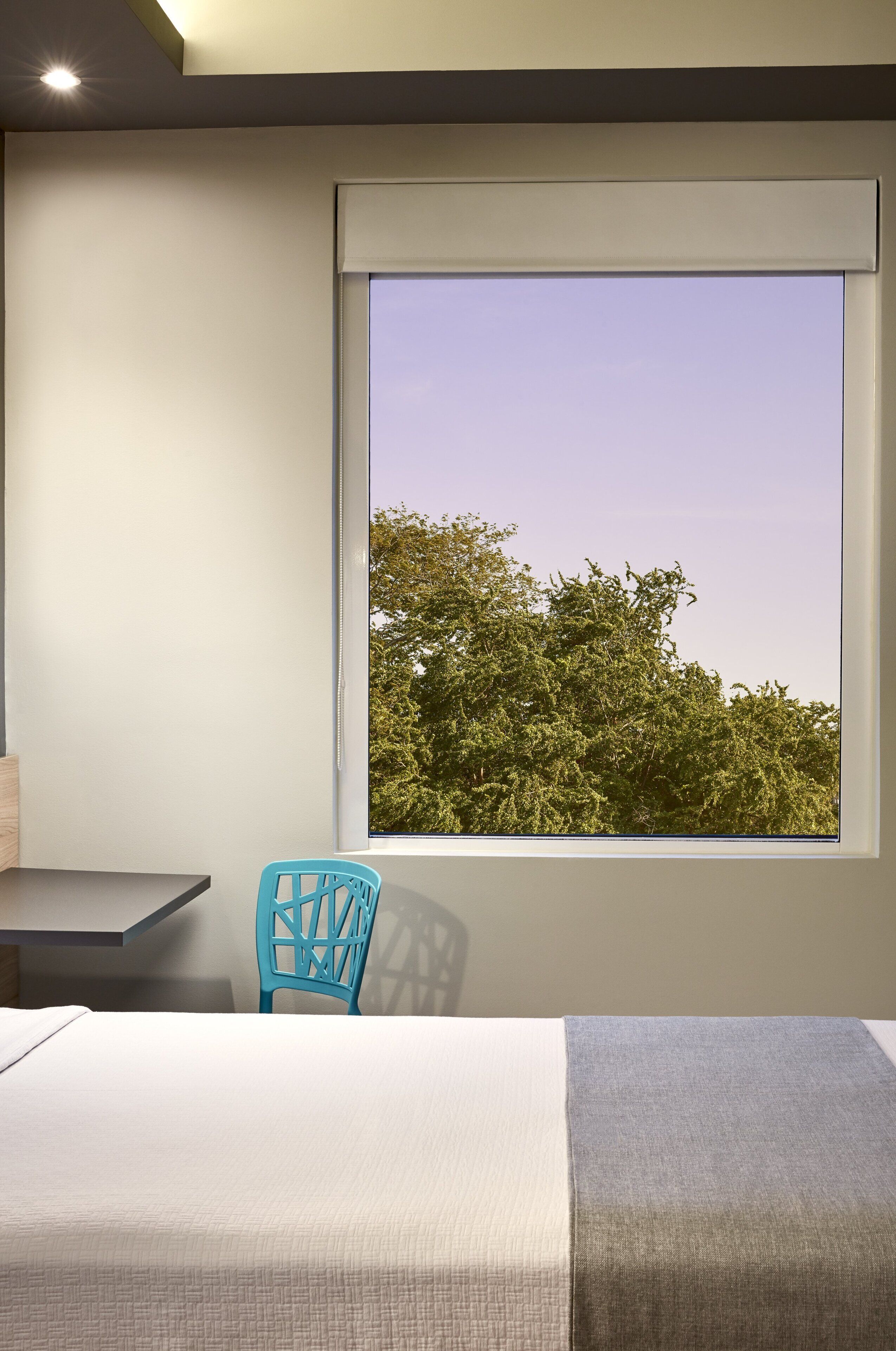 Un dormitorio con cama, una silla, una mesa y una ventana con vistas a árboles.