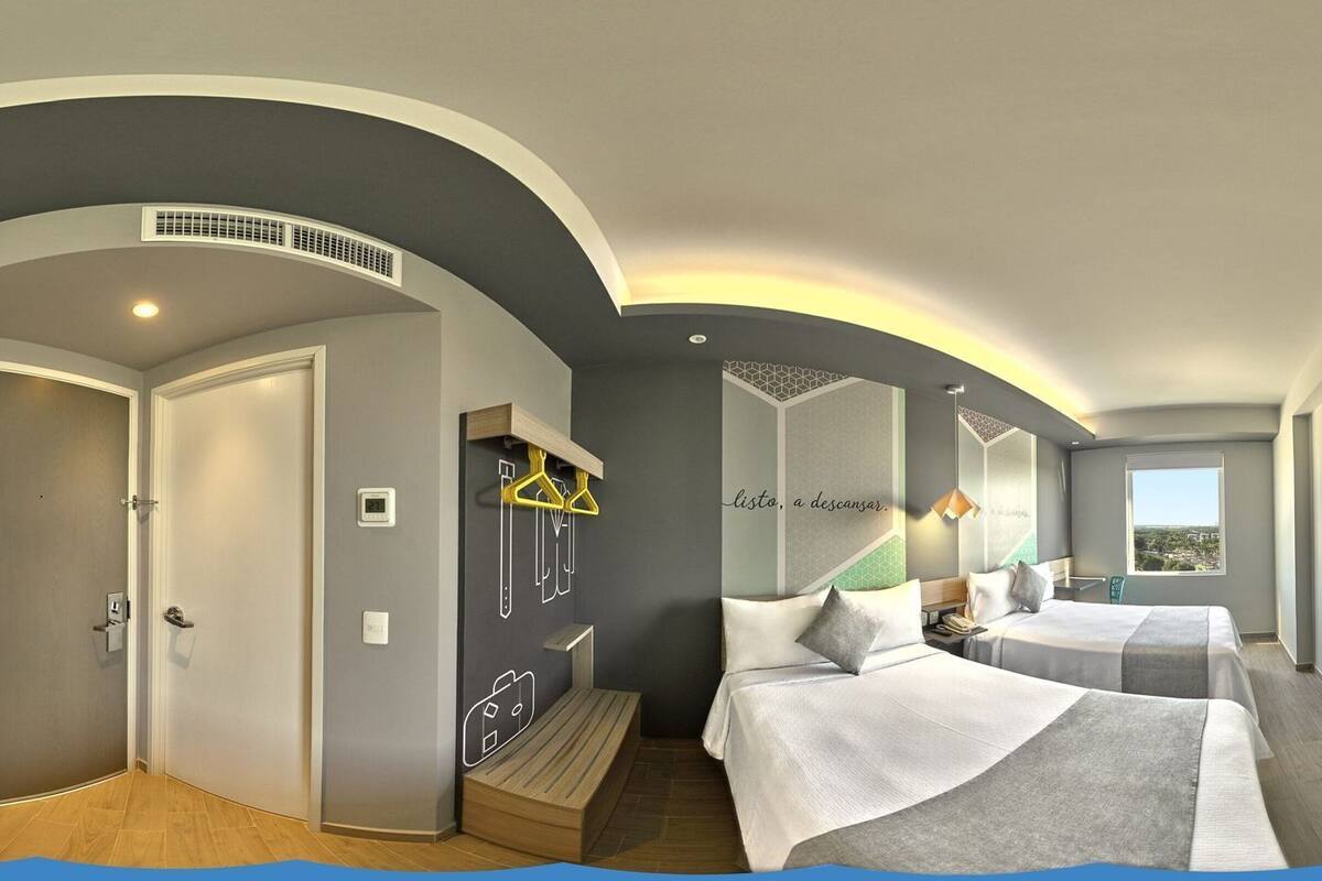 A hotel room with two beds, a desk, a chair, a window with a city view, and a mirror.