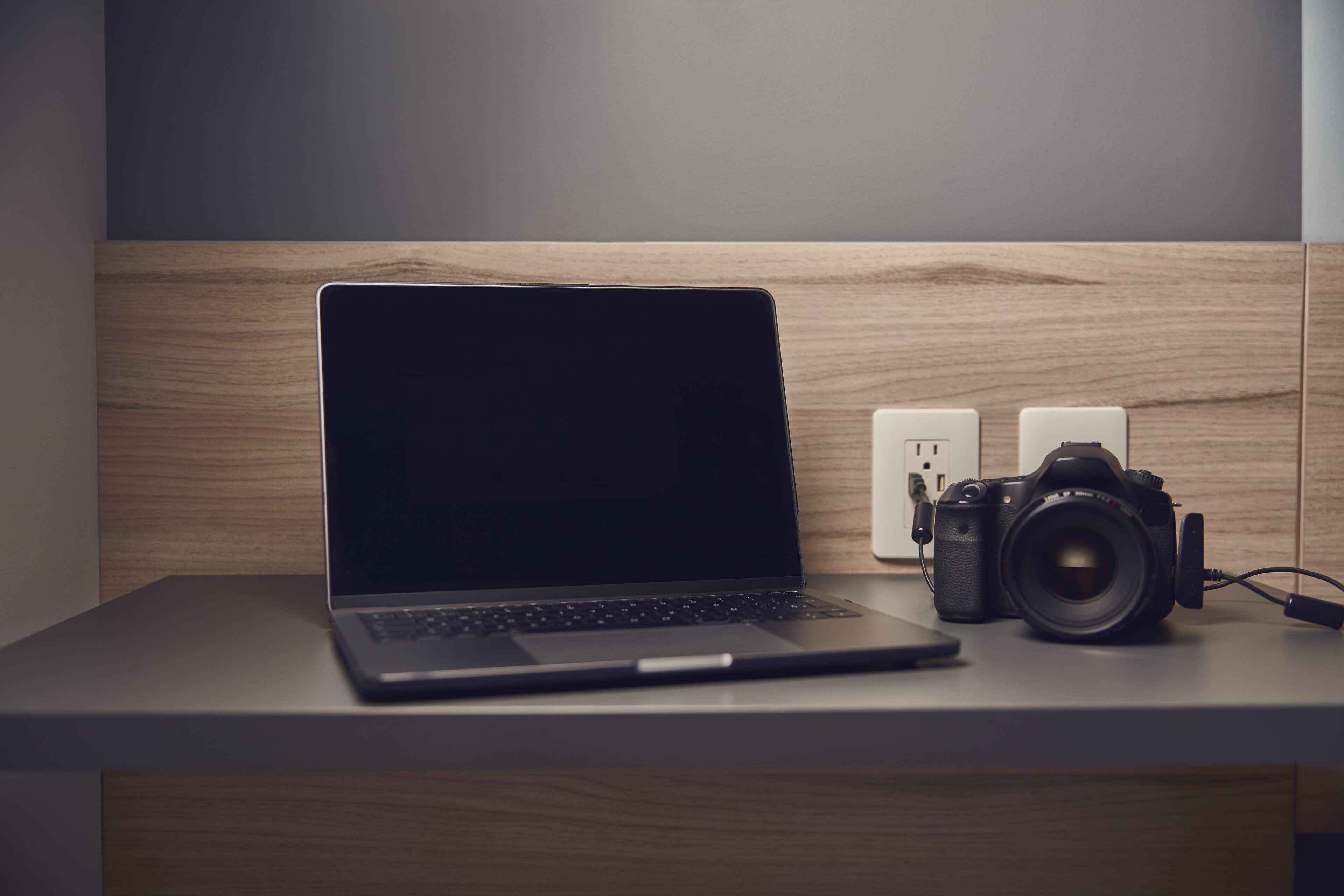 Ein Laptop und eine Kamera liegen auf einem Holztisch mit einer Steckdose.