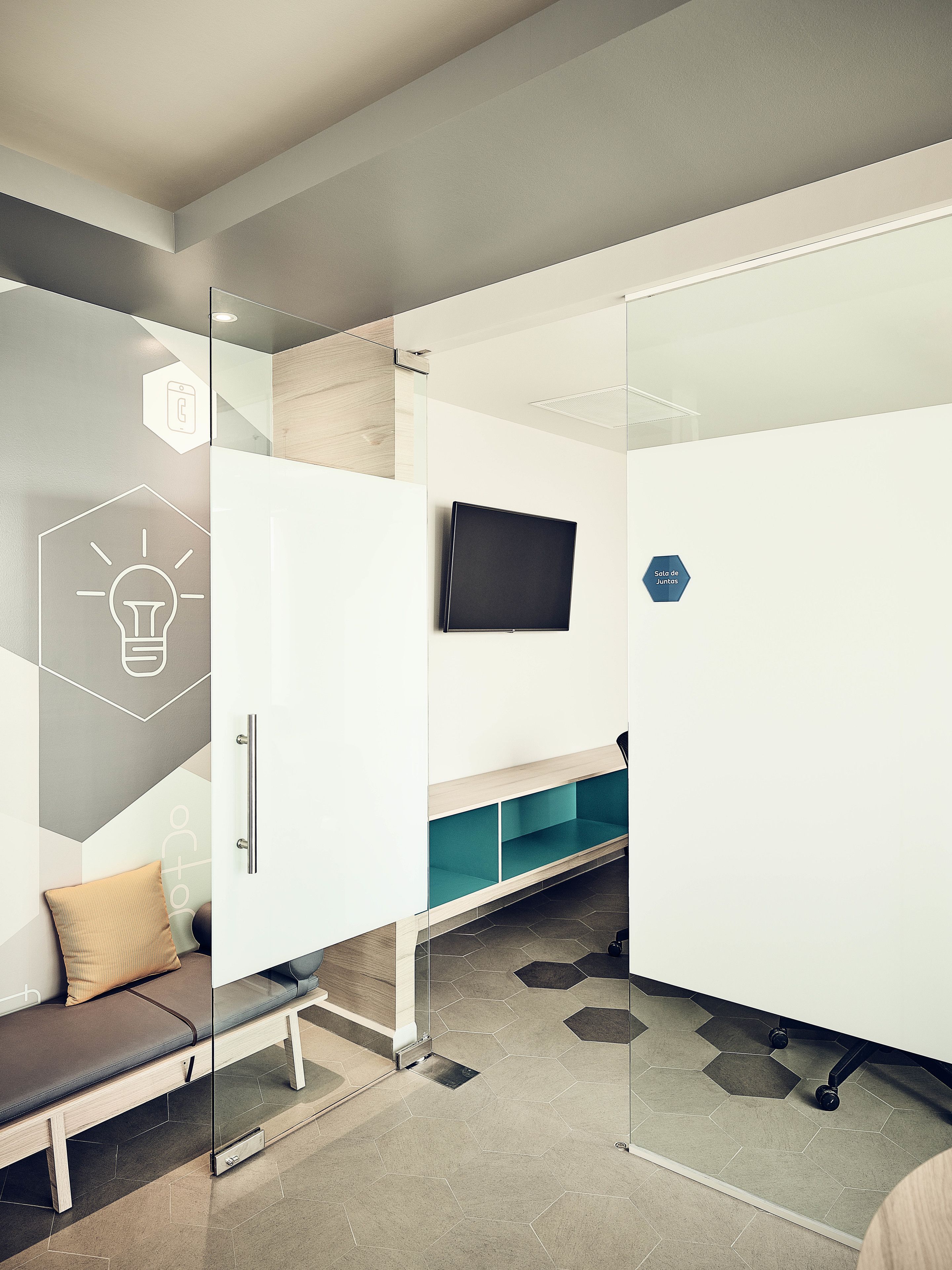 A modern, well-lit room with a bench, a flat-screen TV mounted on the wall, and a storage unit with a glass door.