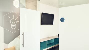 A modern, well-lit room with a bench, a flat-screen TV mounted on the wall, and a storage unit with a glass door.