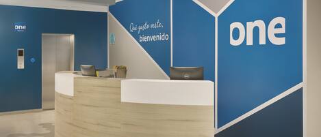 A reception desk with a modern design, a blue accent wall, and a sign that reads "one hotels."