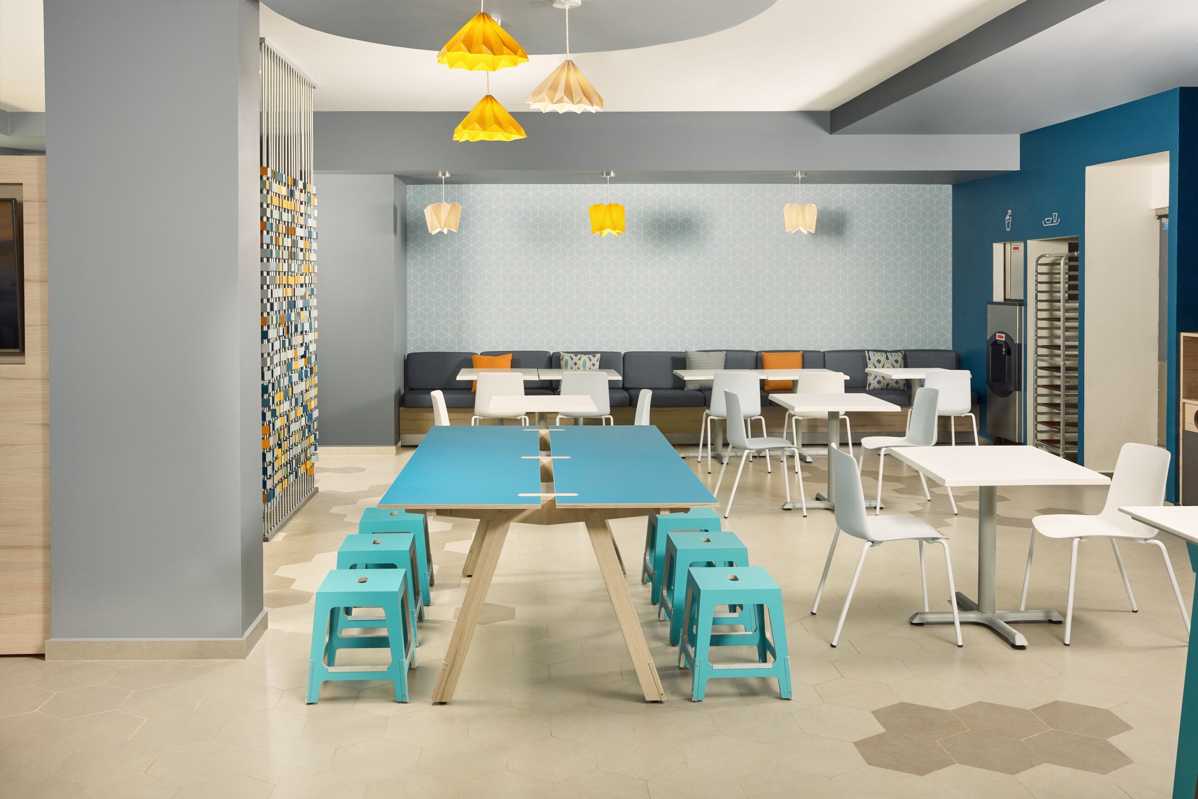 A modern dining area with a long table, multiple chairs, and a seating area with a patterned wall.