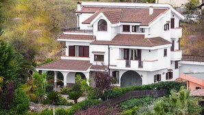 A multi-story white building with a tiled roof, multiple balconies, and a garden area with various plants and a fence. - Domus Dams B&B (Montescaglioso)