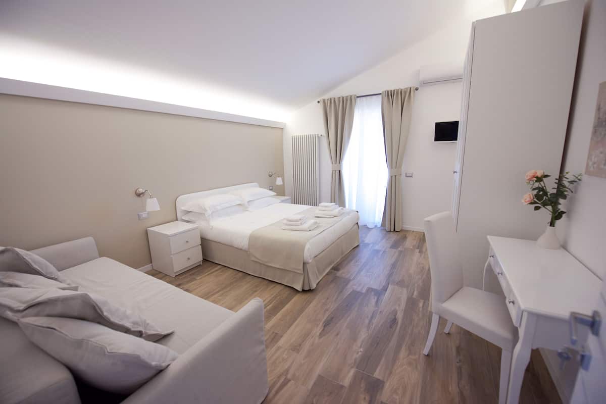 A modern hotel room with a bed, a desk, a chair, and a small table.