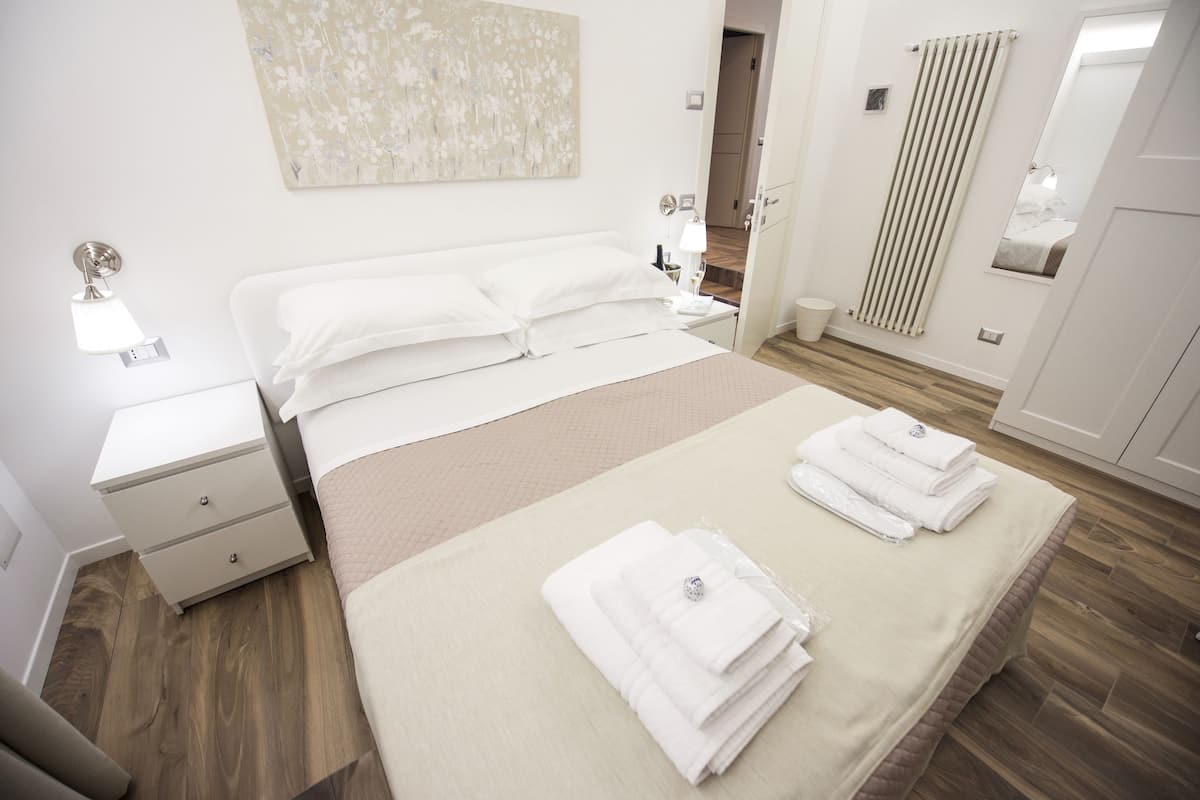 A modern bedroom with a large bed, bedside tables, a nightstand, a mirror, and a radiator.