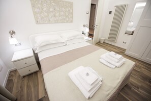 A modern bedroom with a bed, bedside tables, a nightstand, a mirror, a radiator, and neatly folded towels on the bed. - Domus Dams B&B (Montescaglioso)
