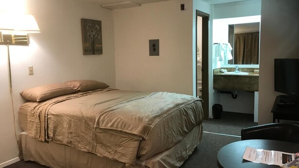 Habitación de hotel con cama, escritorio, lámpara, televisor y baño visible a través de una puerta abierta.