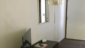 Una habitación con un escritorio de madera oscura, una computadora, un espejo y dos lámparas fijadas a la pared.