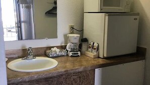 Un baño pequeño con lavamanos, espejo, microondas y cafetera.