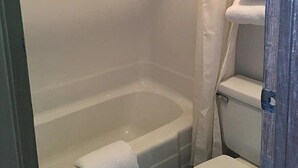Un baño con bañera, inodoro y una pila de toallas blancas.