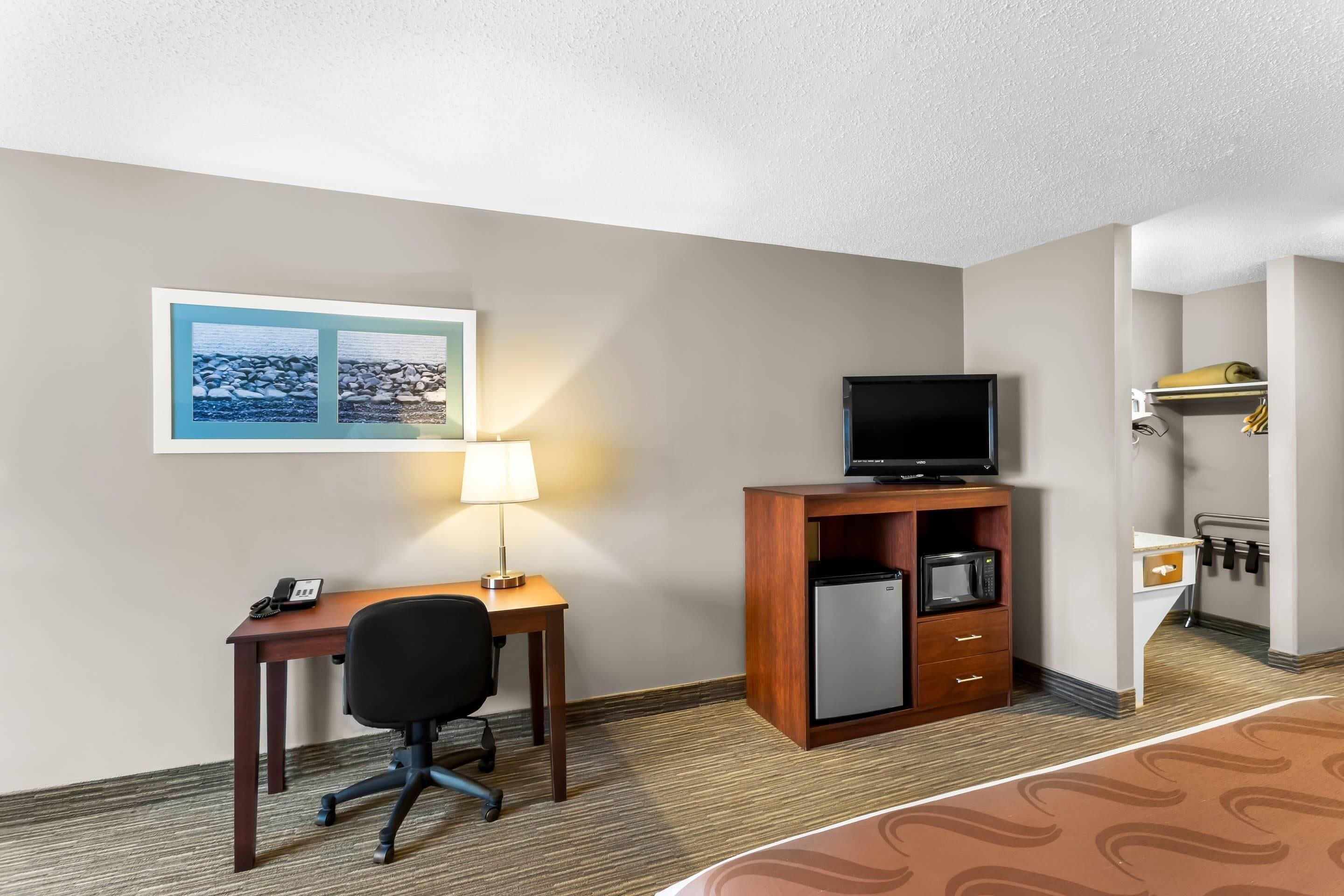 Ein Hotelzimmer mit Schreibtisch, Stuhl, Fernseher, Kühlschrank und einem Bett.
