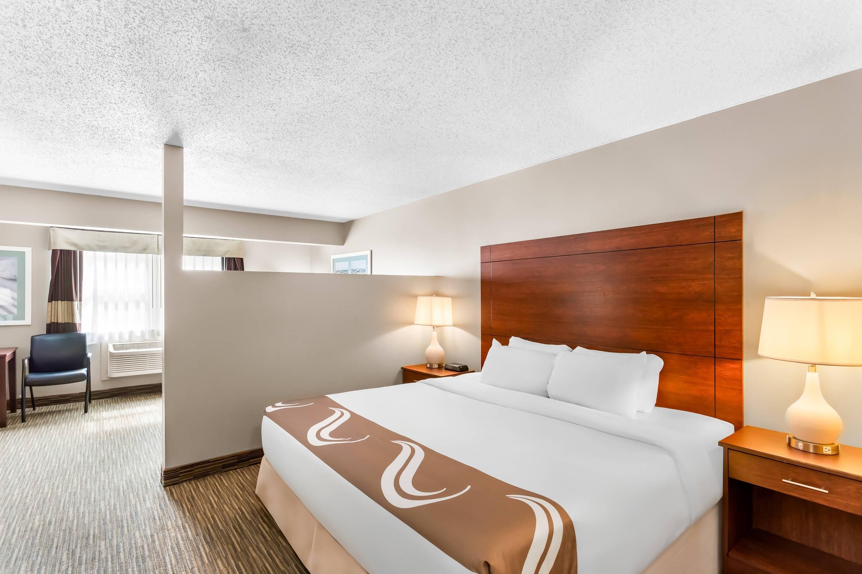 A hotel room with a bed, bedside tables, a chair, and a lamp.