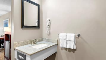 Un baño con lavamanos de granito, un espejo, un secador de pelo y un perchero para toallas.