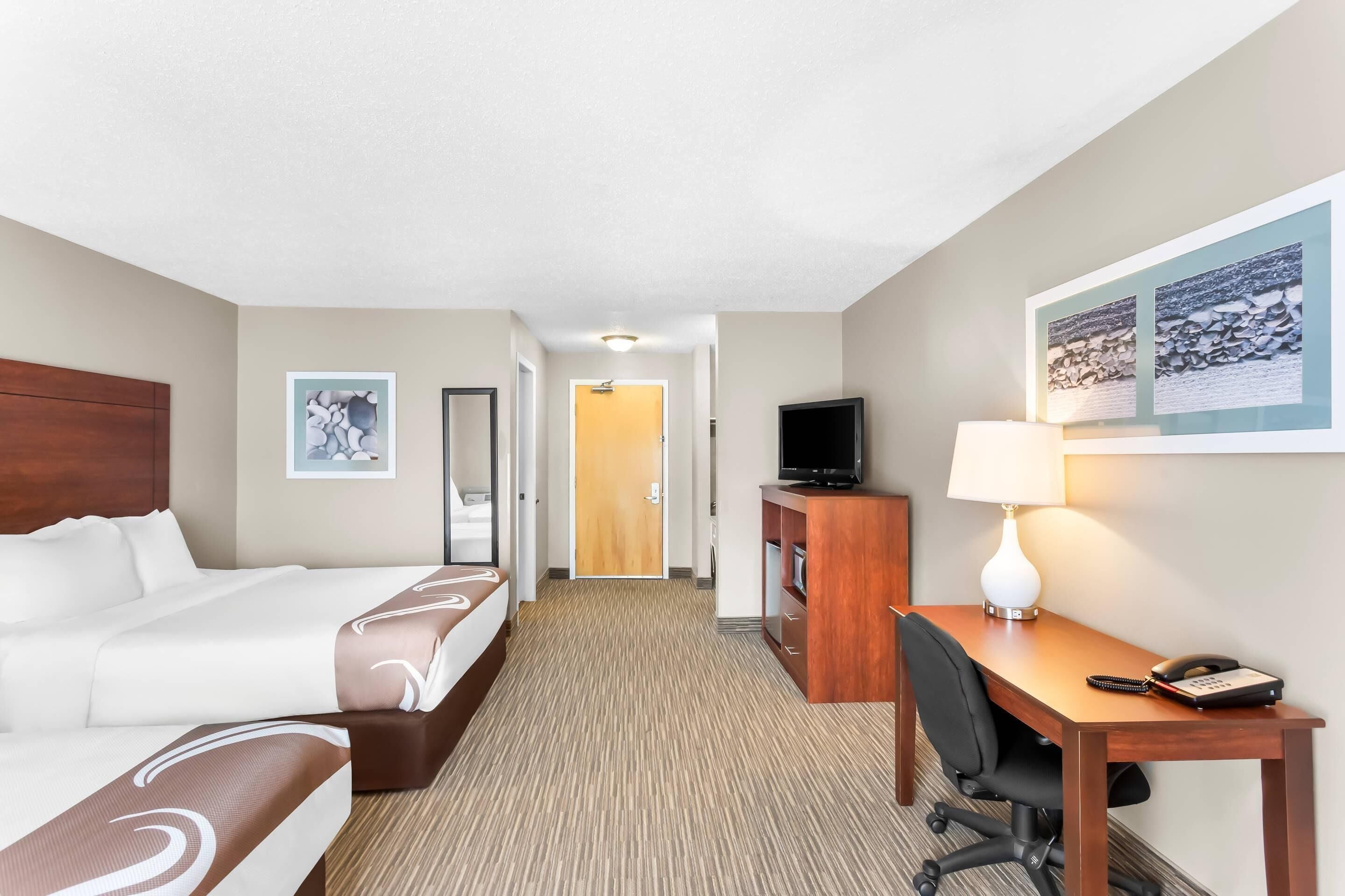 A hotel room with a bed, a desk, a television, and a lamp.