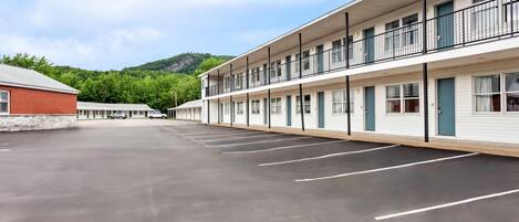 Un motel con un estacionamiento, un edificio de ladrillo a la izquierda y una colina al fondo.