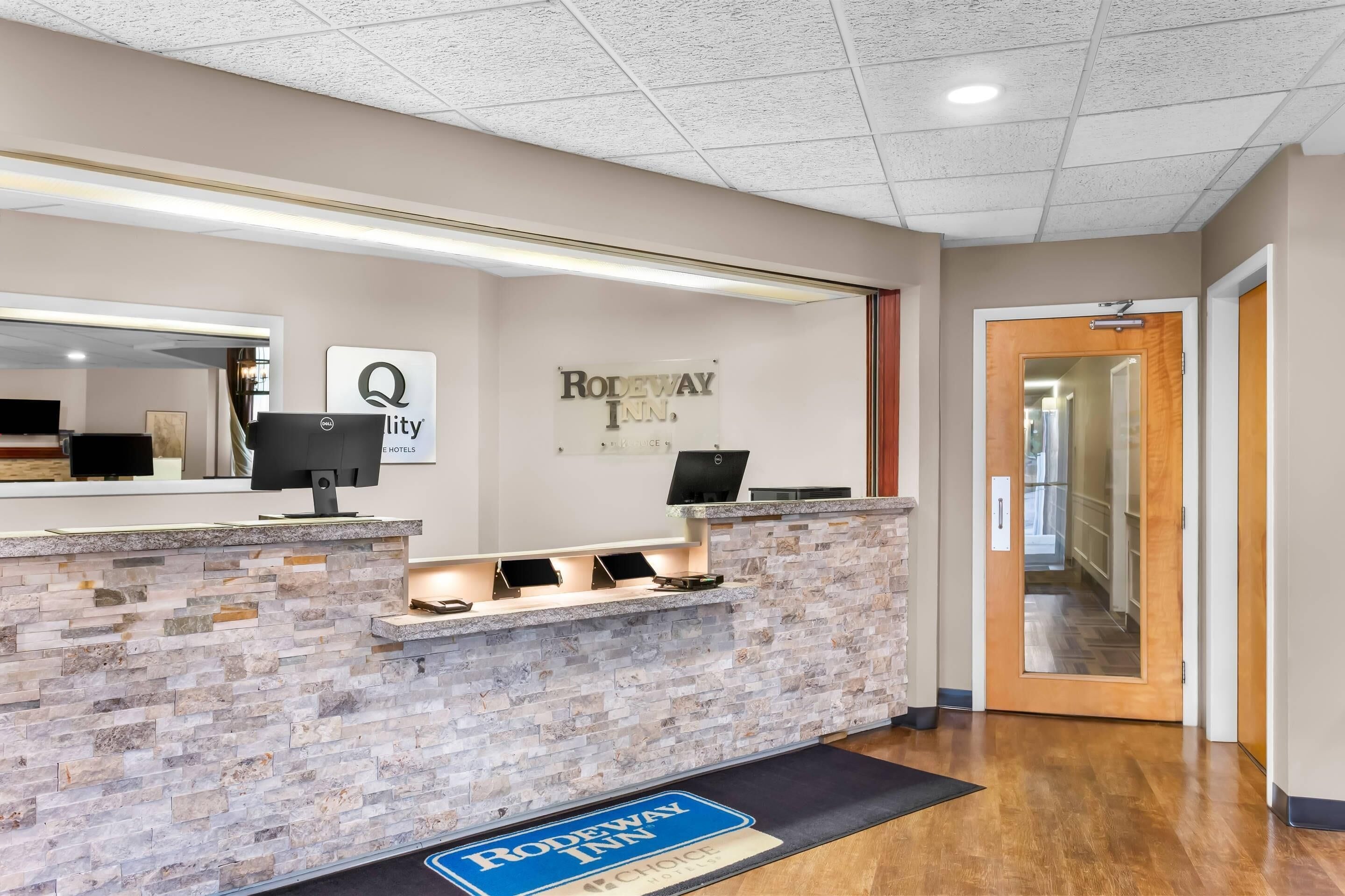 A reception area with a stone counter, a sign for Rodeway Inn, and a reception desk with a computer.