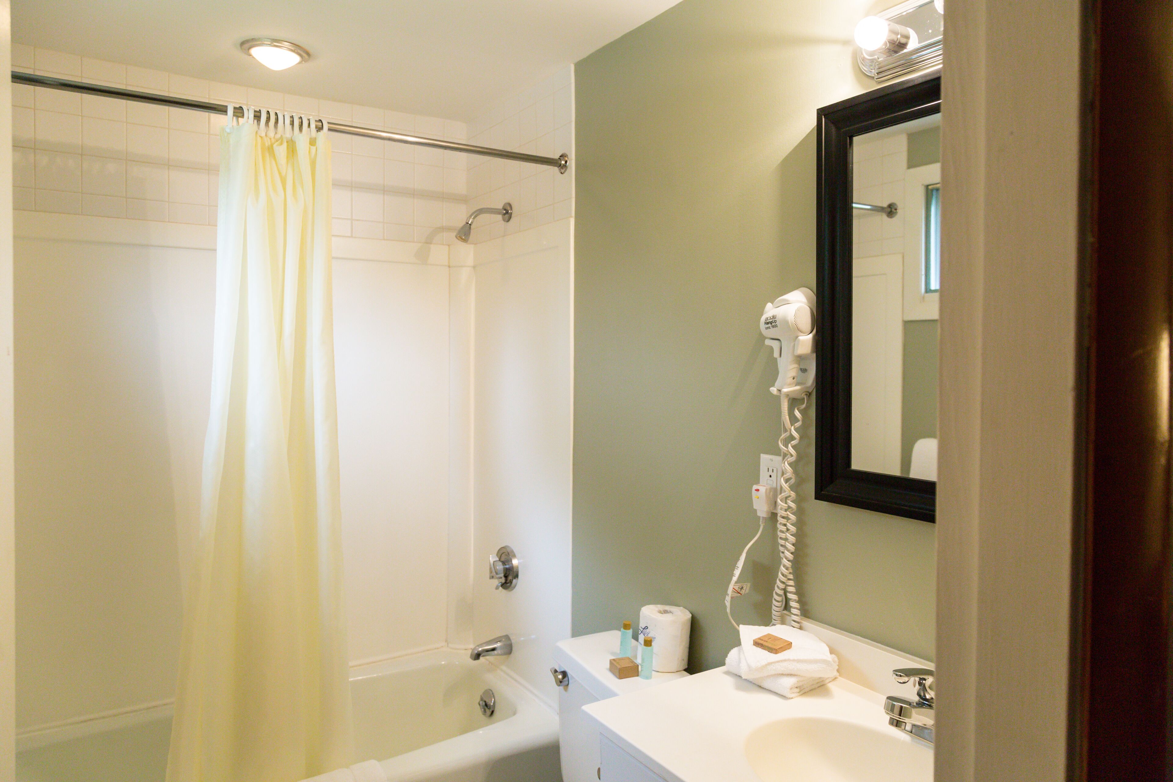 A bathroom with a bathtub, a shower curtain, a toilet, a sink, a mirror, and a hairdryer.