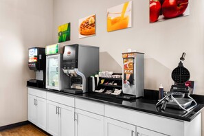 A self-service breakfast station with various food and drink options, including a waffle maker and a coffee machine. - Quality Inn & Suites Gorham Riverside (Gorham)