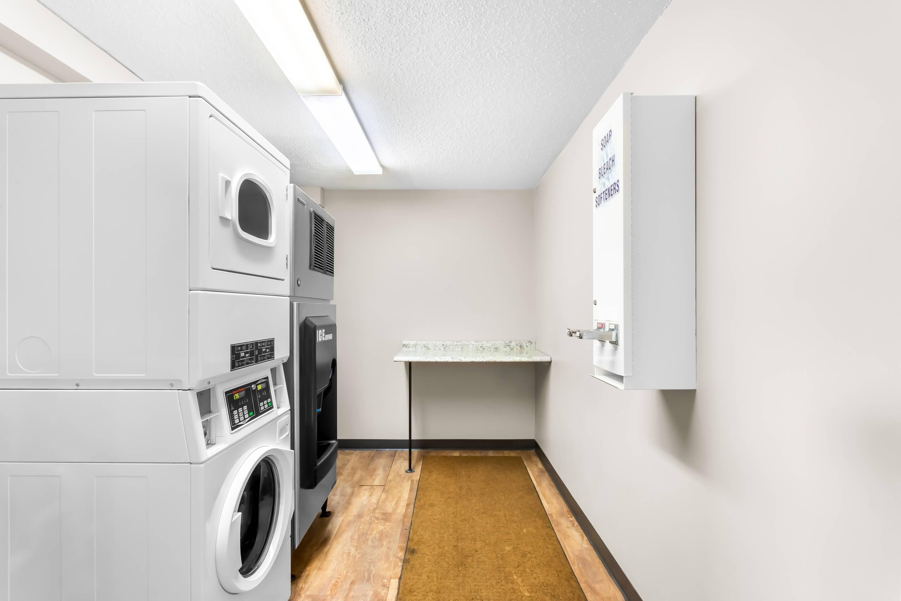 A laundry room with stacked washers and dryers, a small sink, and a whiteboard on the wall.