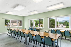A conference room with a long table, chairs, and large windows with a view of a town and mountains. - Quality Inn & Suites Gorham Riverside (Gorham)