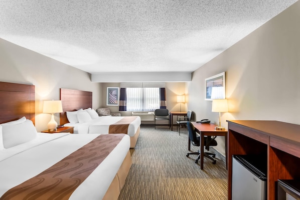 A hotel room with two beds, a desk, a chair, a lamp, a refrigerator, and a window with curtains. - Quality Inn & Suites Gorham Riverside (Gorham)