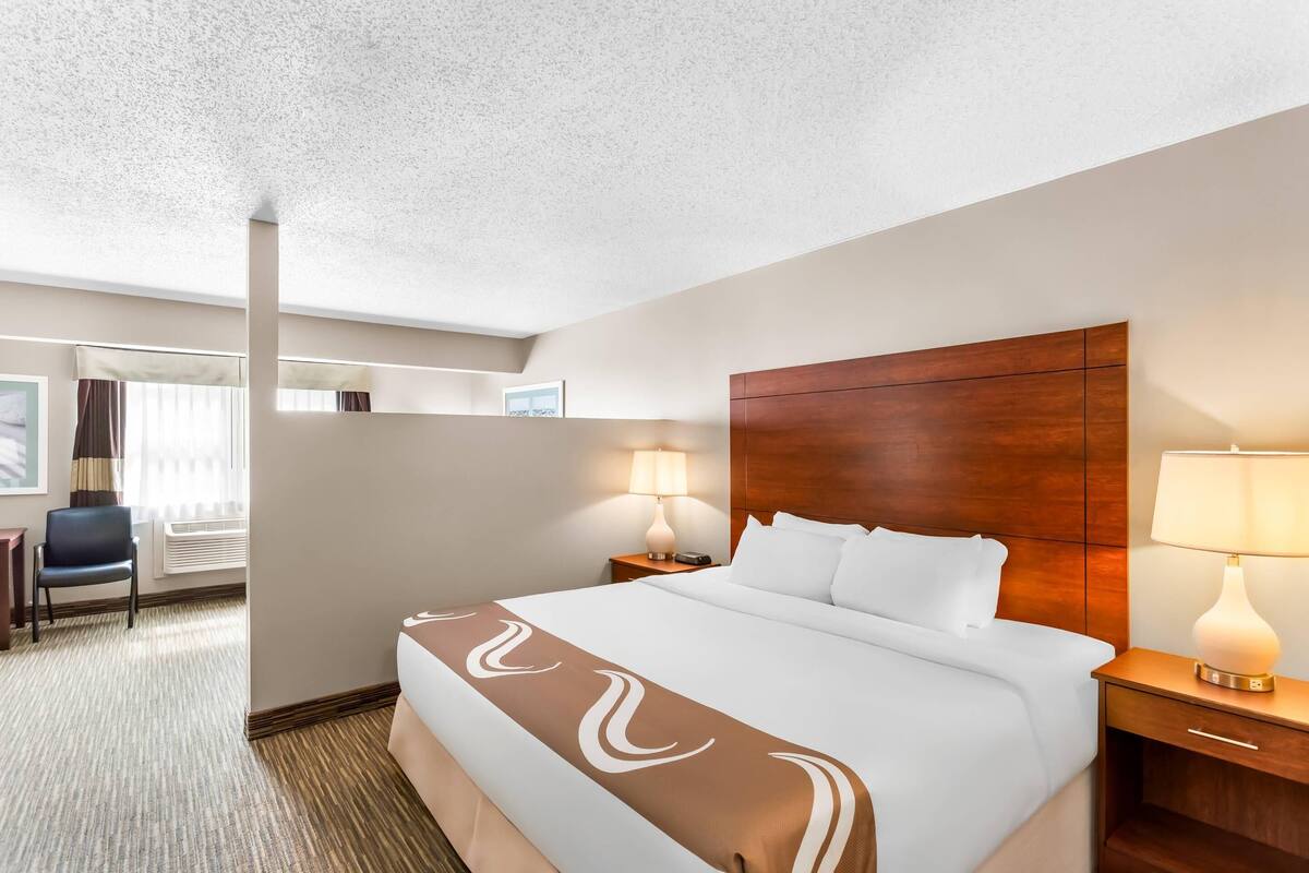 A hotel room with a bed, bedside tables, a chair, and a lamp.