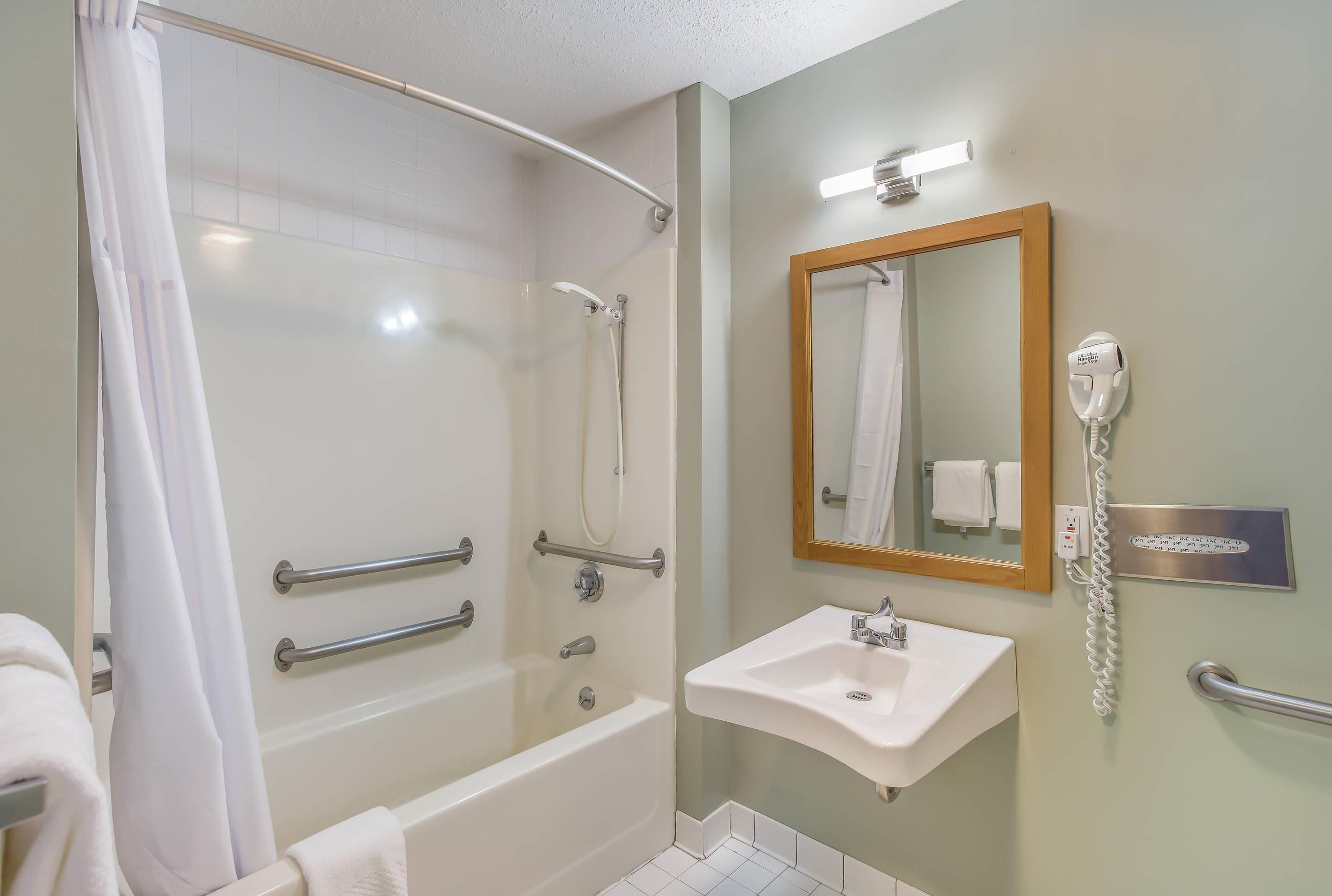 Un baño con bañera, lavamanos, espejo y secador de pelo en la pared.