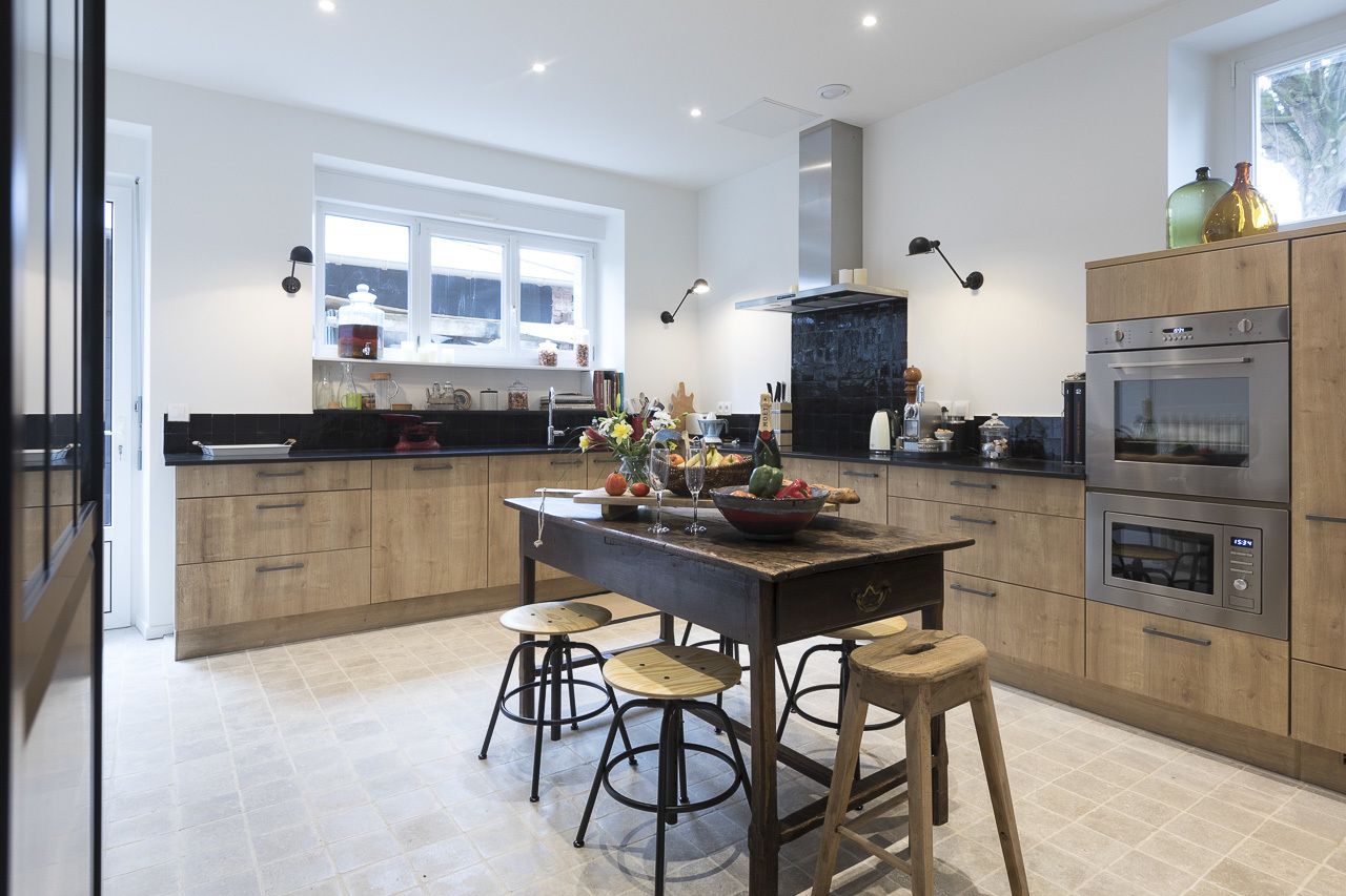 A modern kitchen with wooden cabinets, a central island with stools, stainless steel appliances, and a window providing natural light.