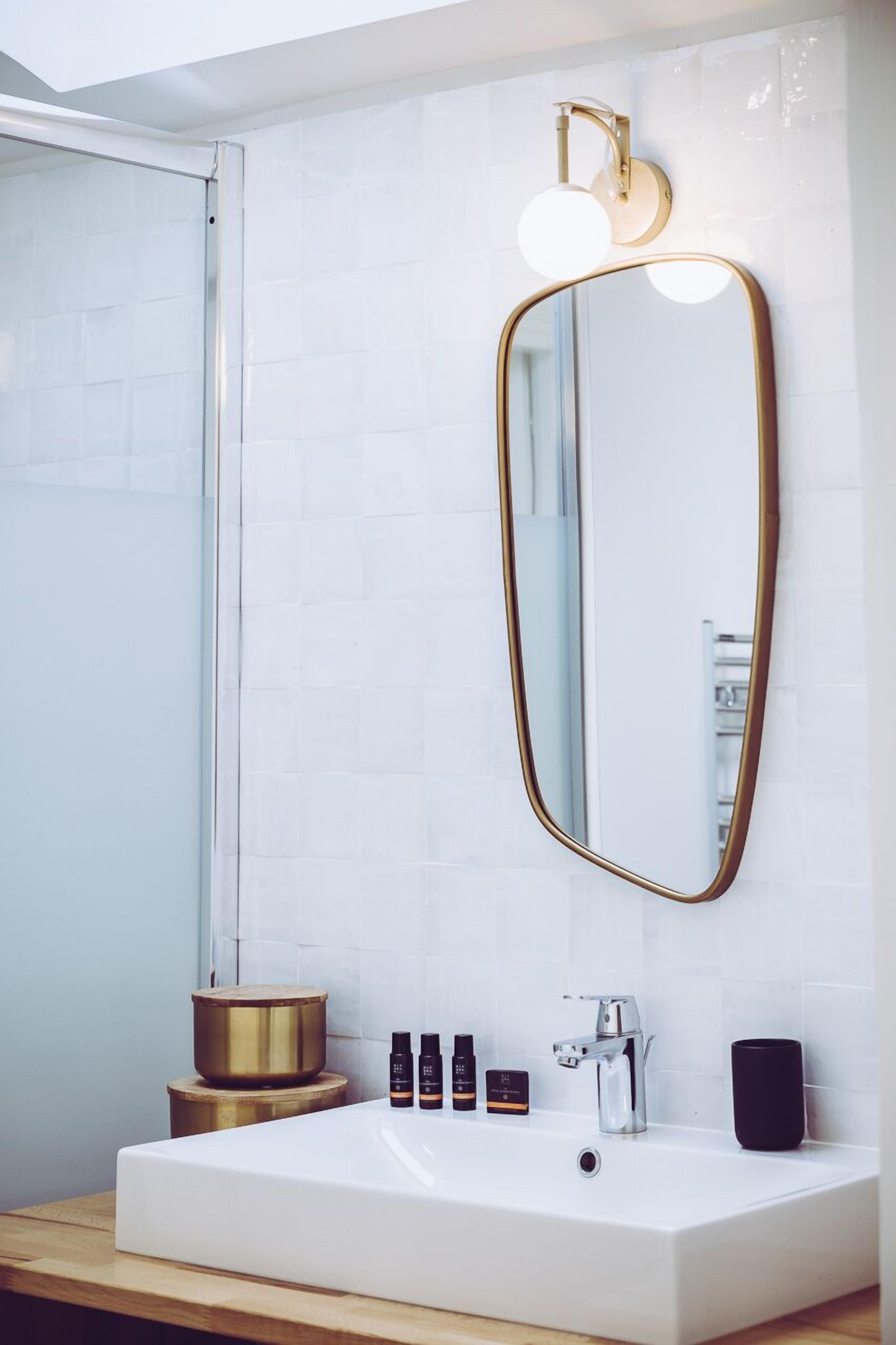 A modern bathroom with a white sink, gold accents, and a large mirror.