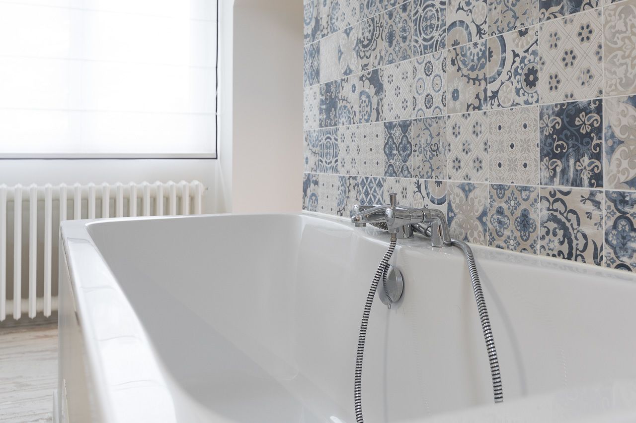 Un baño moderno con una bañera independiente, un radiador blanco y azulejos estampados en la pared.