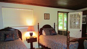 A bedroom with two beds, a nightstand with a lamp, and a window with blinds. - Yearling Restaurant and Cabins (Hawthorne)