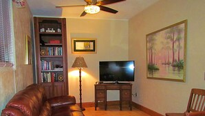 A living room with a leather sofa, a TV on a wooden stand, a lamp, a bookshelf, and a painting on the wall. - Yearling Restaurant and Cabins (Hawthorne)