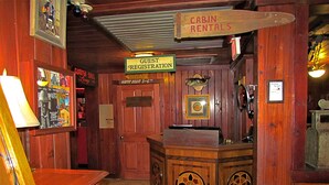 A wooden cabin rental area with a guest registration desk, a sign for cabin rentals, and a sign indicating happy hour hours. - Yearling Restaurant and Cabins (Hawthorne)