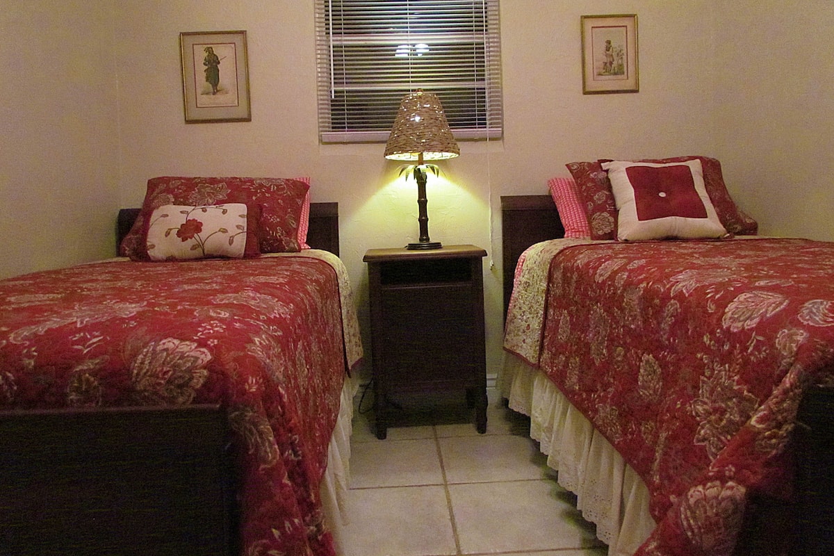 A bedroom with two beds, a nightstand, a lamp, and two framed pictures on the wall.