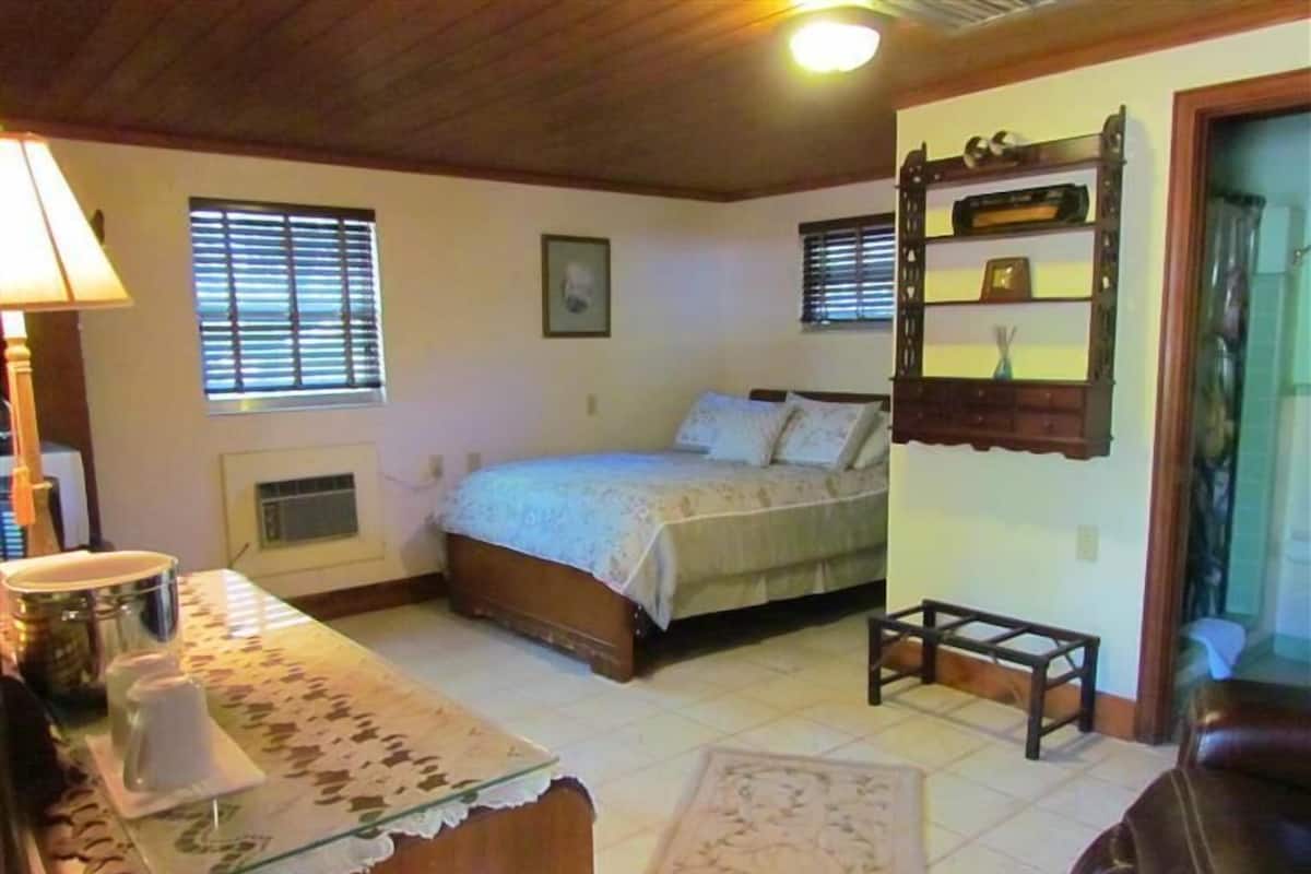 A bedroom with a bed, bedside table, lamp, and a window with blinds.