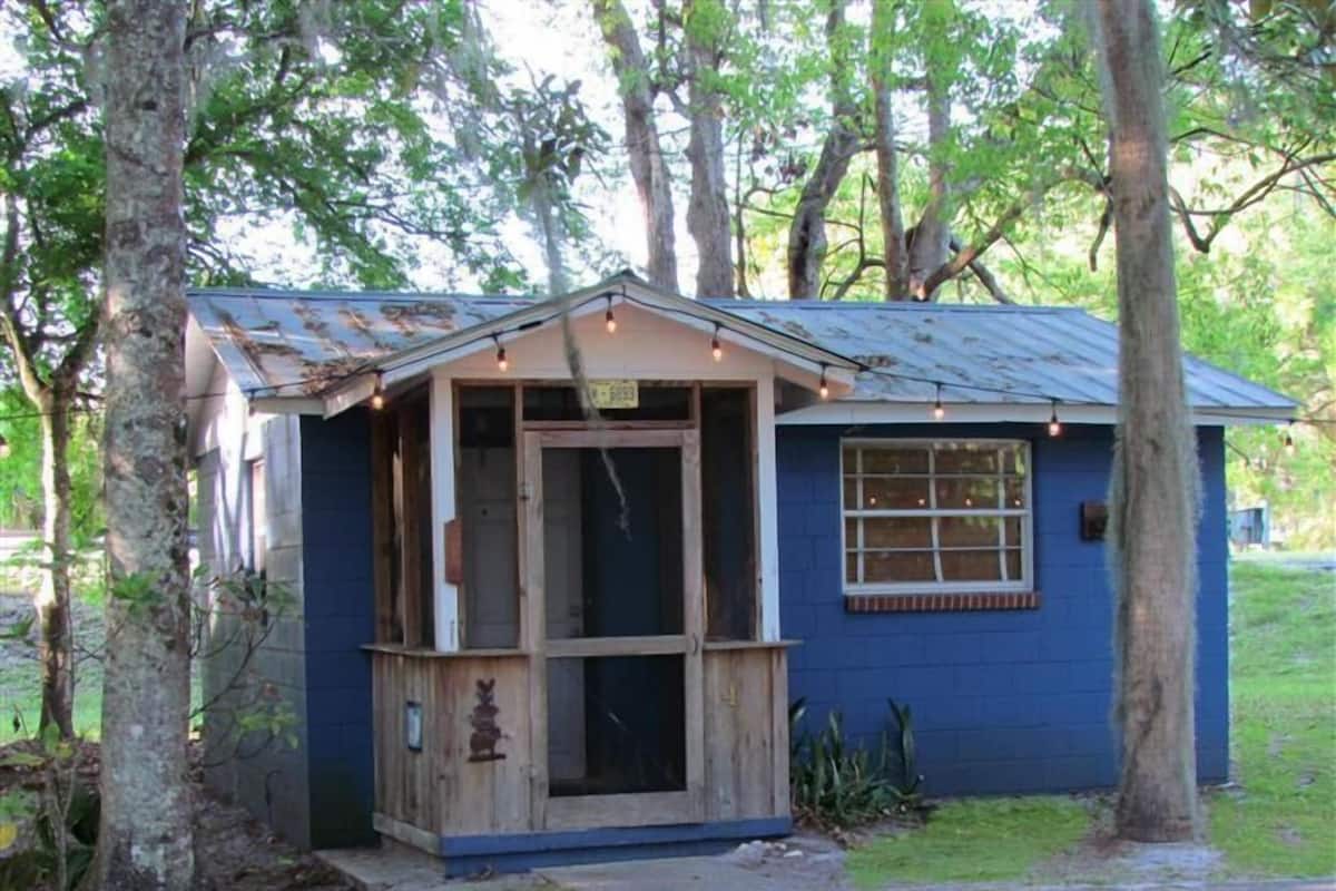 A small, single-story building with a blue exterior, a wooden door, and a window.