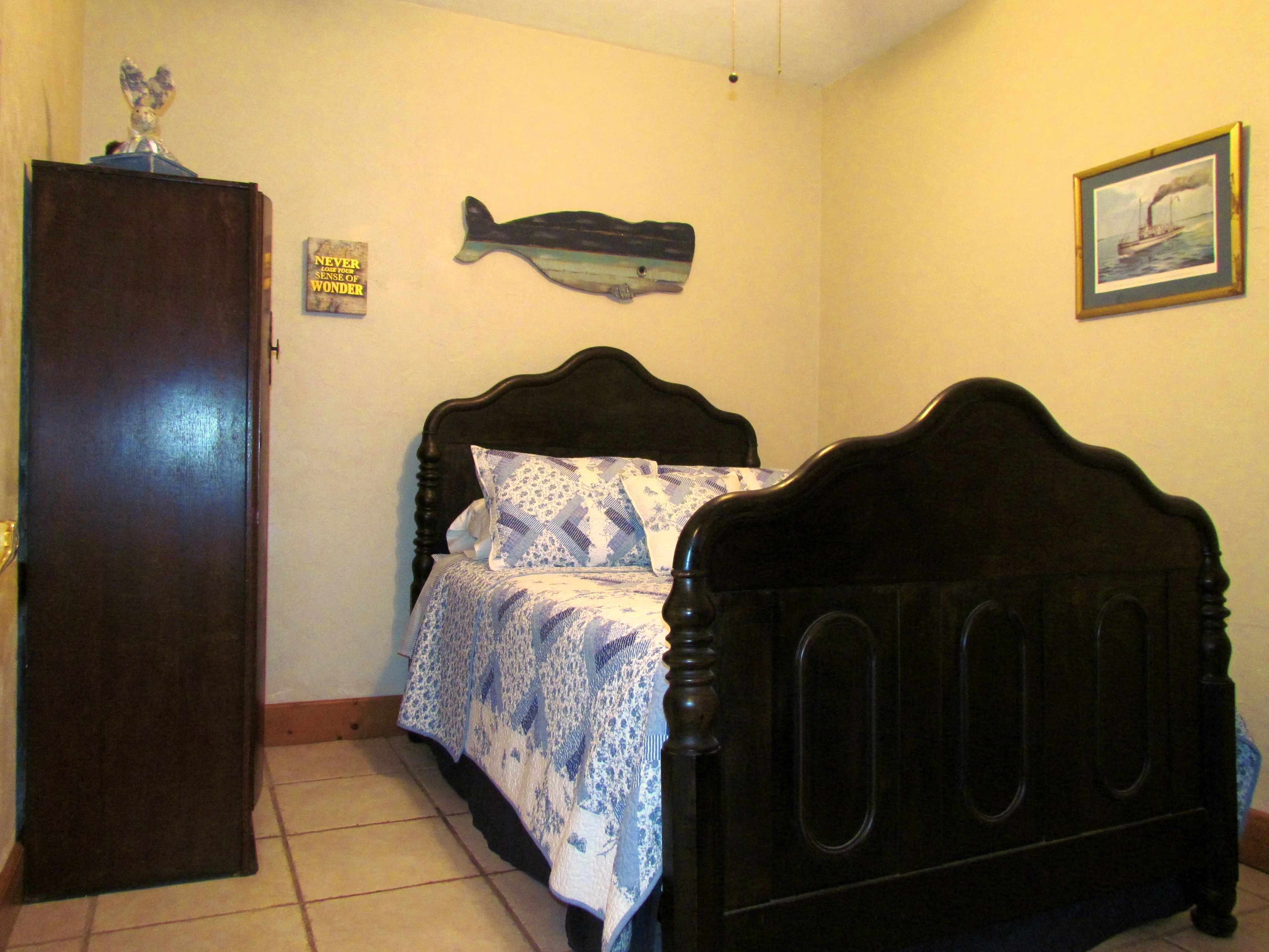 A bedroom with a bed, a wooden wardrobe, a wall-mounted fish decoration, a framed picture, and a sign.