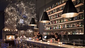 A bar area with wooden chairs, a stone fireplace, and shelves of liquor bottles. - Hidden Pond (Kennebunkport)