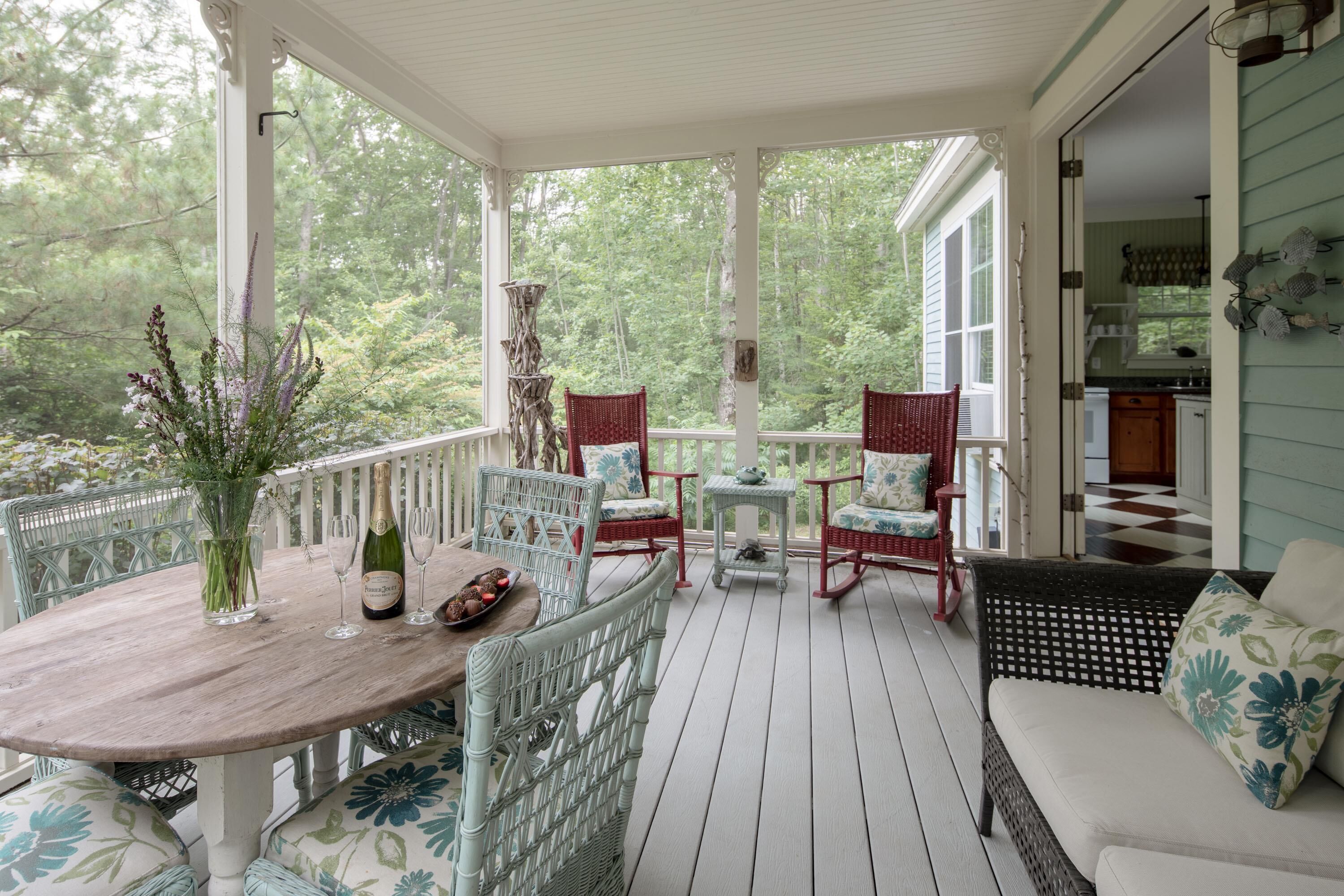 A covered porch with wicker furniture, a wooden table, and a vase with flowers.