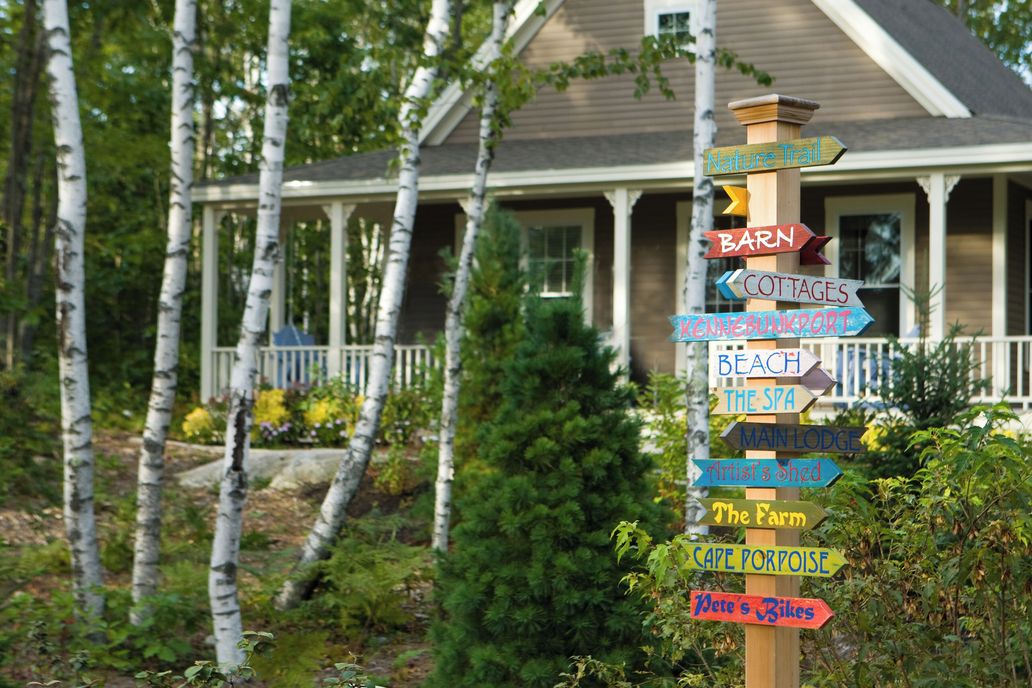 A wooden signpost with multiple directional signs pointing to various local attractions such as a nature trail, barn, cottages, beach, spa, main lodge, artist's shed, the farm, cafe porpoise, and bikes.