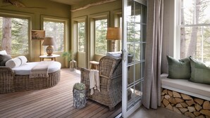 A cozy room with wicker furniture, a ceiling fan, and large windows offering a view of trees. - Hidden Pond (Kennebunkport)