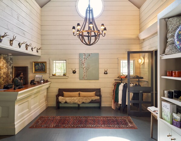 A room with a wooden ceiling, a chandelier, a bench, a rug, and a clothing rack.
