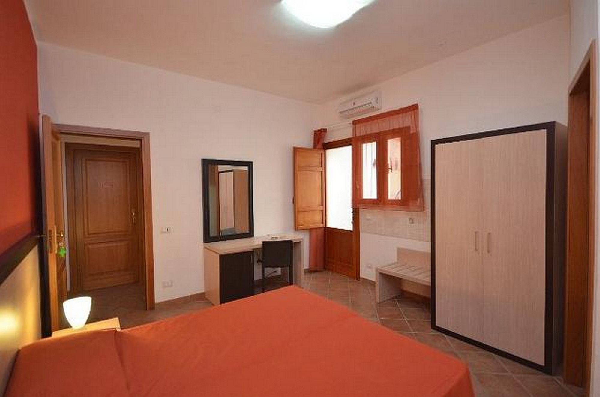 A bedroom with a bed, a desk, a wardrobe, and a window.
