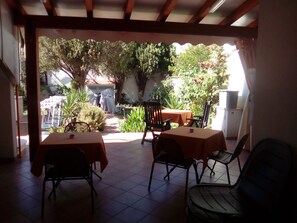 An outdoor patio area with two tables and chairs, surrounded by greenery and a view of a house. - Sigiuma B&B (San Vito Lo Capo)