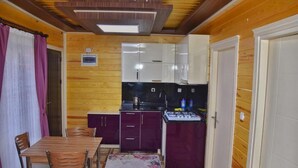 Una cocina compacta con paredes de madera, un comedor con mesa y sillas, y un refrigerador pequeño.