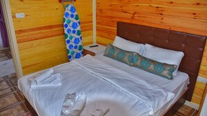 Una cama bien hecha con sábanas blancas, cabecera marrón y una toalla azul y verde con estampado colgando en una pared de madera.