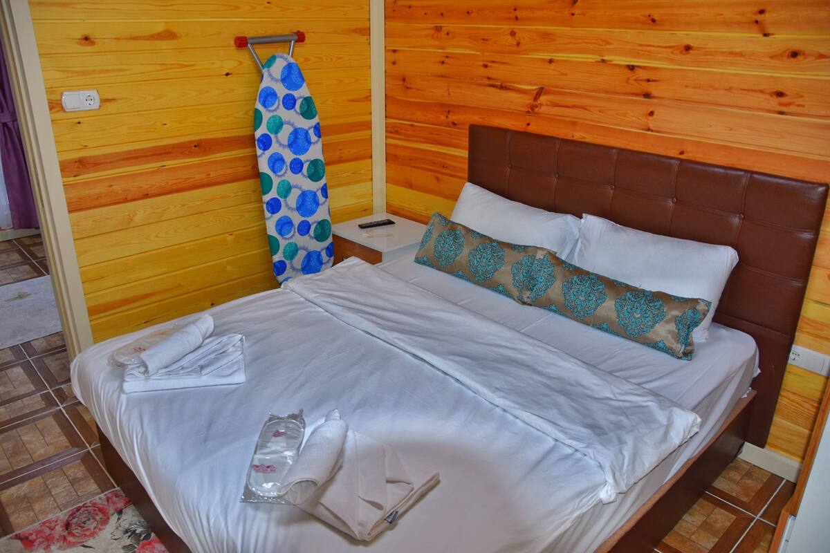 A neatly made bed with white linens, a brown headboard, and a blue and green patterned towel hanging on a wooden wall.