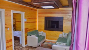 Una habitación acogedora con paredes de madera, un televisor de pantalla plana montado y una cama con colcha verde y blanca.