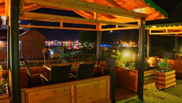 Terraza de madera al aire libre con asientos y macetas, con vista a un paisaje urbano nocturno.